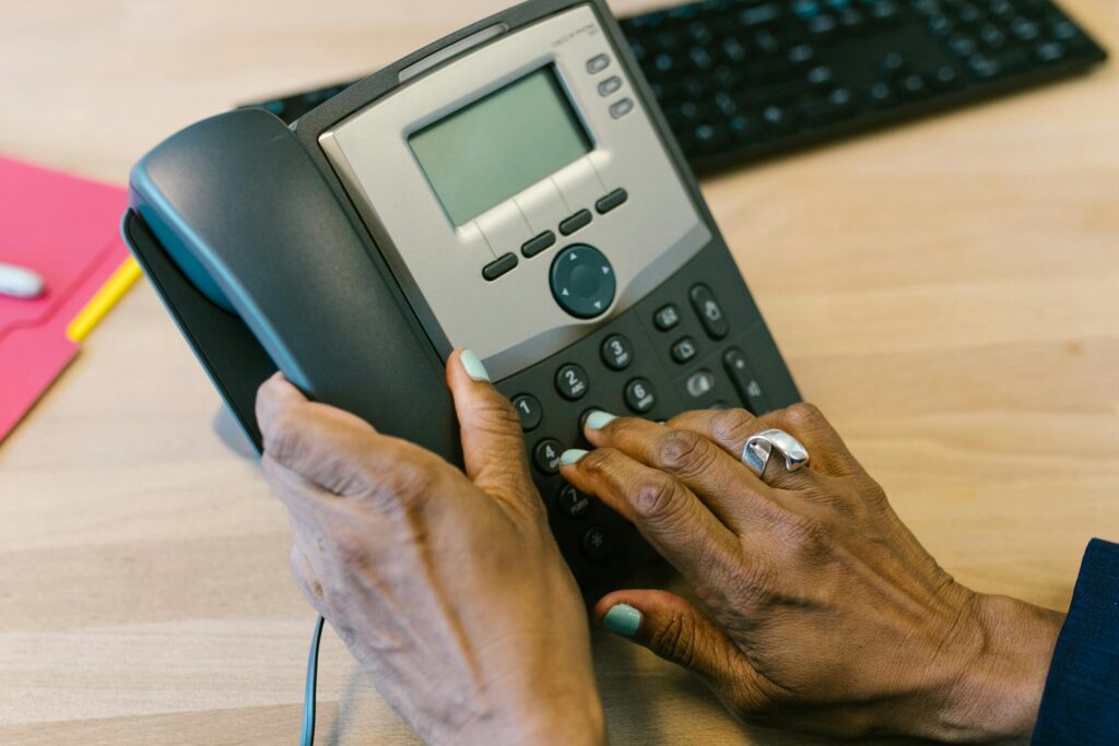 Close-up of hands dialing a desk telephone in an office setting.